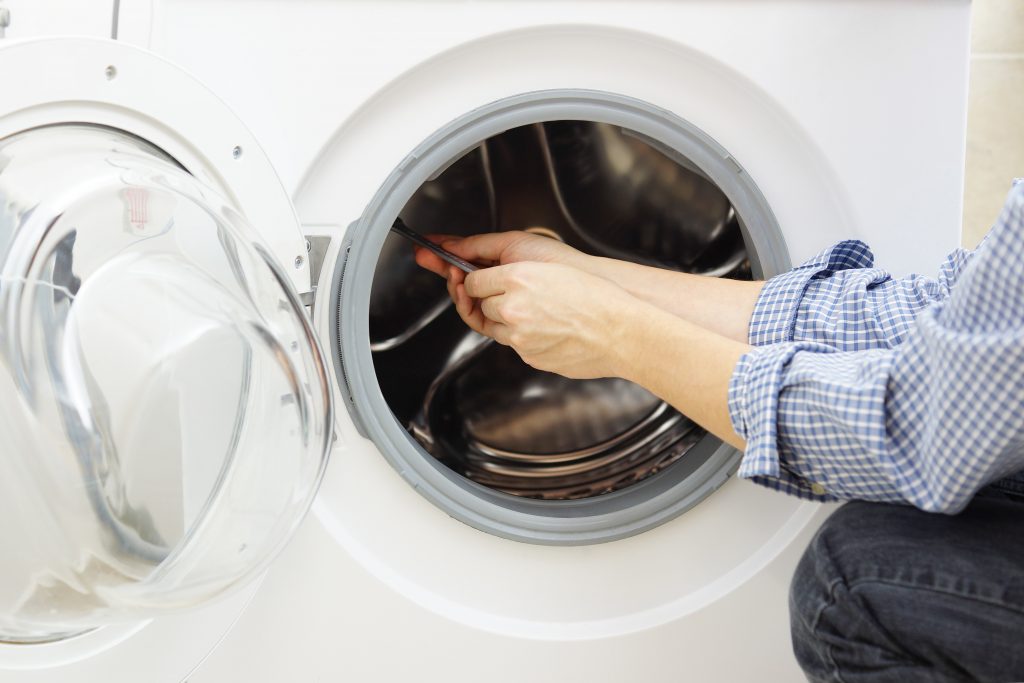 A technician in a blue shirt repairing a clothes dryer